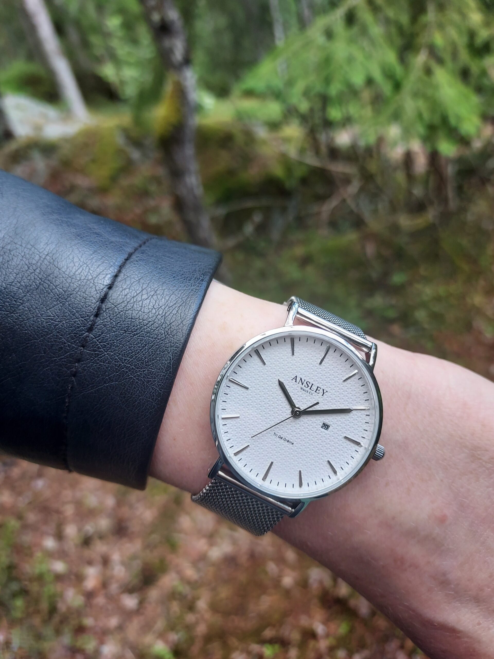 Ansley watch in forest Ansley Watch worn on wrist in a forest setting, featuring a clean white dial with minimalist design and stainless steel mesh band.
